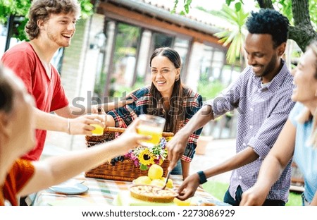Young men and women toasting healthy orange fruit juice at farm house pic nic - Life style friendship concept with multicultural friends having fun together on afternoon relax time - Bright filter