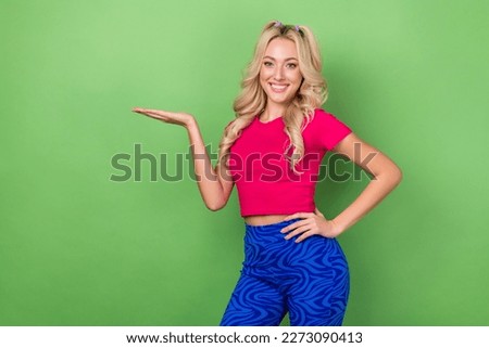 Photo of cheerful young gorgeous lady curly blonde hairstyle hold palm demonstrate new product advertisement isolated on green color background