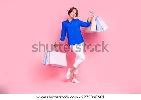 Full body photo of young satisfied lady wear blue shirt white trousers hold shopping bags enjoy new outlet center isolated on pink color background