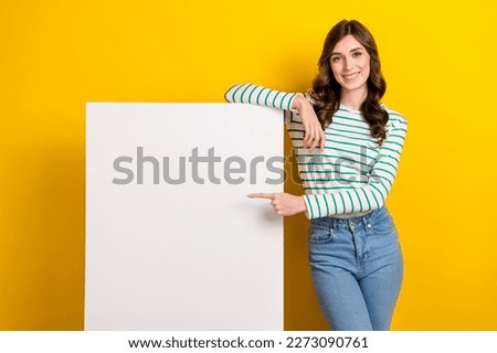 Photo of optimistic cute girl with wavy hairdo dressed striped shirt directing at white wall board isolated on yellow color background