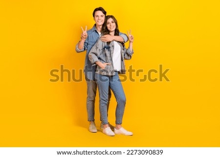 Full length photo of sweet pretty couple wear jeans showing v-signs cuddling isolated yellow color background