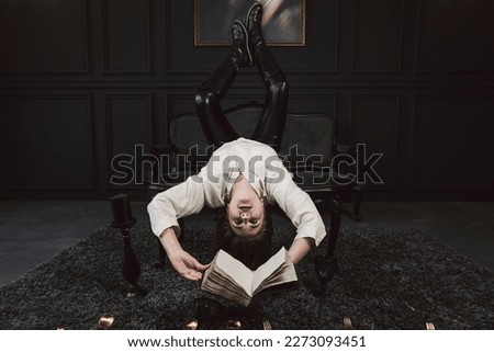 Portrait of a Mystical or magical girl with a gothic make-up and auburn hair, dressed in a off-white shirt. Posing in a dark gothic room with gilded cutlery and book in the hands.