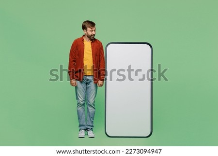 Full body smiling elderly man 40s years old wears casual clothes red shirt t-shirt look at big huge blank screen mobile cell phone smartphone with area isolated on plain pastel light green background