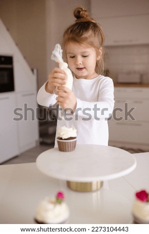 Cute funny baby girl 4-5 year old making cupcakes at kitchen table at home. Little child cooking cakes. Childhood. 