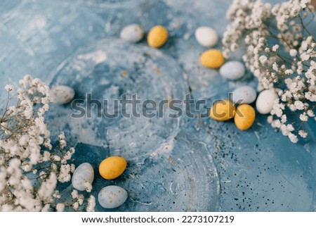 Blue, yellow, white eggs and white small flowers lie on a beautiful blue and turquoise picturesque background. Spring Background for Easter