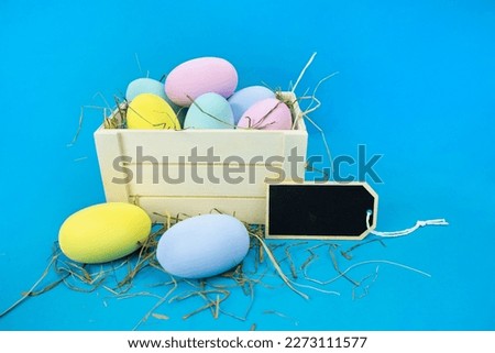 Easter moc-up. Wooden box with straw and colorful eggs on a blue background. Holiday concept, congratulation, postcard, template,copy space, text, handmade,spring,decoration,party,poster,symbol,sale. Royalty-Free Stock Photo #2273111577