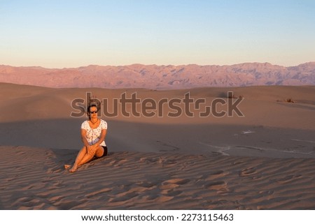 Touristic woman enjoying the sunrise with scenic view on Mesquite Flat Sand Dunes, Death Valley National Park, California, USA. Morning walk in Mojave desert with Amargosa Mountain Range in back.