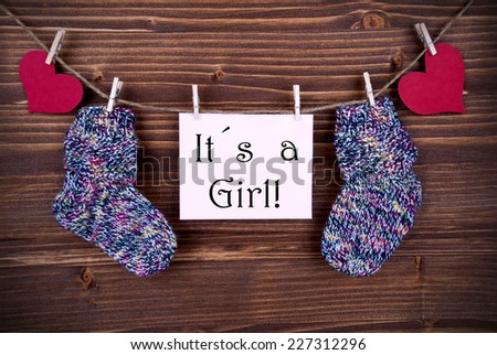 Baby Sockets and red Heart Hanging on a Line together with a Label on which stands It's a Girl
