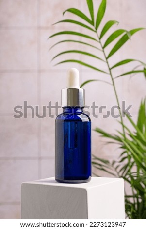 Mockup of skincare cosmetic product. Blue bottle of eco or natural serum on white cube pedestal with green plant on bathroom background