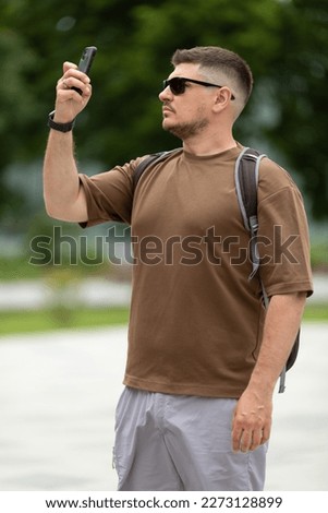 A male tourist in sunglasses takes pictures of the sights on his phone