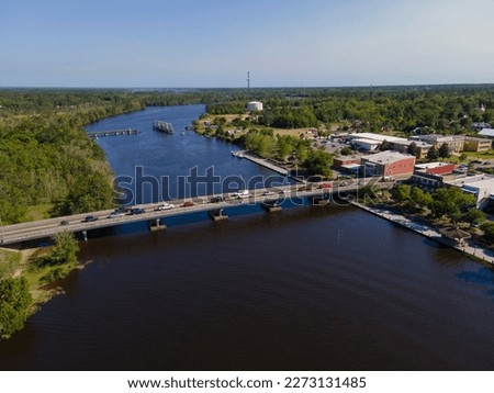 Aerial shot of highway bridge and swing bridge over the wide river at Milton, Florida. Land area with trees on left and buildings on the right connected by two bridges over the river. Royalty-Free Stock Photo #2273131485