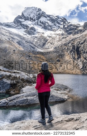 Young woman looking at landscape with snowy mountains and blue lake in Laguna Churup, Cordillera Blanca, Parque Nacional Huascaran, Huaraz - Peru