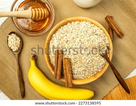 Rolled oats or oat flakes in bowl with wooden spoons, banana, honey, Cinnamon sticks and bottle of milk on background. Healthy lifestyle, healthy eating concept
 Royalty-Free Stock Photo #2273138595
