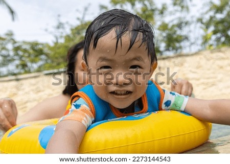 Portrait image of An Asian kid happy and enjoying playing water on pool with Kids' inflatable swim ring