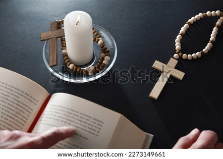 Christian believer reading bible on black nightstand with religious items for prayer with christian cross open bible and lighted candle on glass plate