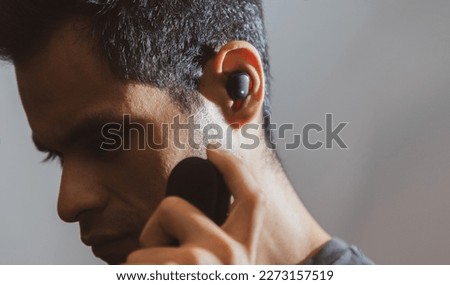 A young Latino man with brown skin wearing headphones and listening to music against a neutral background with colorful lighting effects