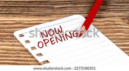 Word NOW OPENING on paper with ped pencil on wooden background