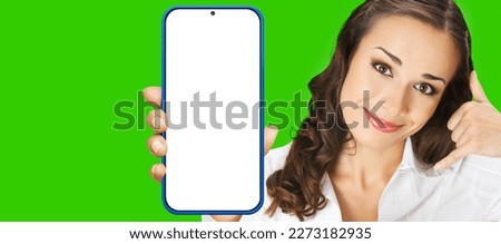Portrait image of smiling confident woman showing call me gesture, holding smartphone cell phone mobile with white blank mock up screen, isolated green chroma key background.