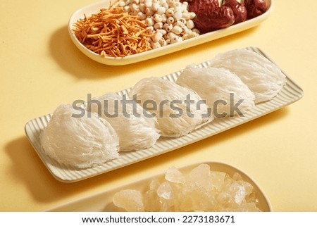 Raw bird's nest is arranged on a long rectangular plate, herbs with cordyceps, lotus seed, jujube and rock sugar are on beige background. Food good for health, increase resistance and anti-aging. Royalty-Free Stock Photo #2273183671