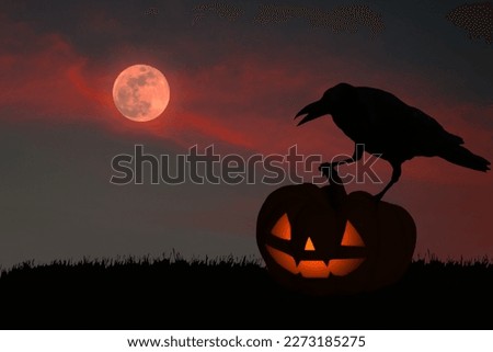 Silhouette of a crow standing on a yellow pumpkin carved as a Halloween devil face in a red full moon sky setting.