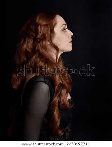  close up portrait of beautiful woman with long red hair wearing sheer corset top, variety of emotional expressions.  Isolated on dark studio background with. Moody silhouette lighting. Royalty-Free Stock Photo #2273197711