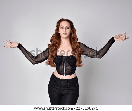  close up portrait of beautiful woman with long red hair wearing black corset top, gestural hands poses, arms reaching out as if casting a spell.   Isolated on dark studio background with. Moody silho