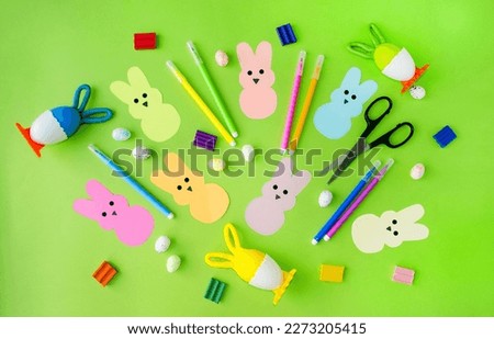 On a green background, Easter pepps bunnies cut out of colored paper, felt-tip pens, colored eggs, scissors, plasticine.  Flat lay, top view.  Concept craft, applique, children's creativity.