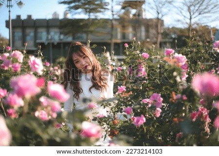 A beautiful asian woman wearing a white dress poses with a rose at rose garden in Taiwan.