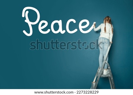 Child girl on ladder writing word Peace on the wall with brush. Social, peace, environment, world concept