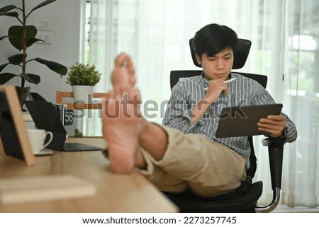 Image of asian male freelancer in smart casual wear using digital tablet at modern home office