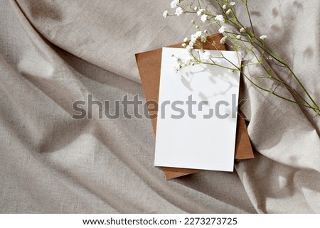 Minimalist floral wedding invitation or greeting card, postcard template, blank paper card and flowers on a beige neutral linen background