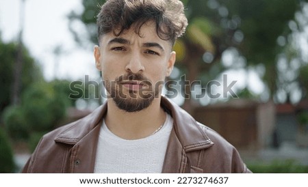 Young arab man standing with serious expression at park Royalty-Free Stock Photo #2273274637