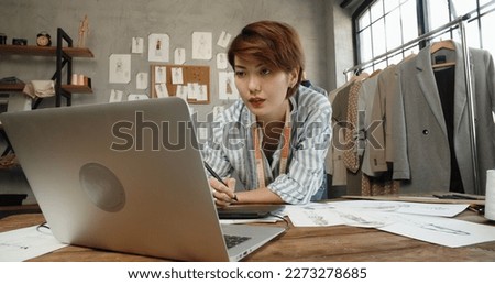 Hipster asian clothes designer working with her sketches, drawing them on graphics tablet, designing her new collection - small business, fashion concept 