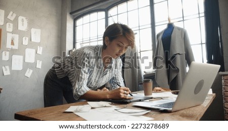 Hipster asian clothes designer working with her sketches, drawing them on graphics tablet, designing her new collection - small business, fashion concept 