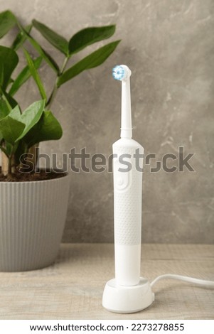 Electric toothbrush with green flower on grey background. Vertical photo. Top view