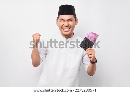Excited handsome young Asian Muslim man holding wallet of full cash money isolated on white background. People religious Islamic lifestyle concept Royalty-Free Stock Photo #2273280571