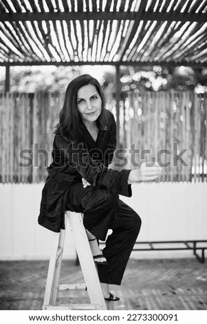 Concept Self made brunette business woman in black business suit filling positive emotions, smiling and enjoying the moment, having fun, sitting on stepladder Black and white