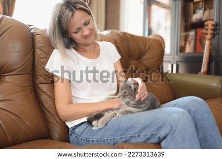 Woman with gray cat on her lap sits on sofa. Concept of enjoyment, pet care and peace. Royalty-Free Stock Photo #2273313639