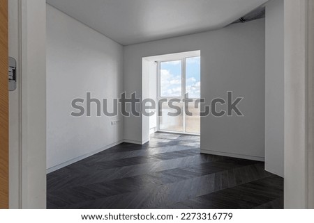 Empty apartment with large floor-to-floor window overlooking nature and blue sky with clouds.