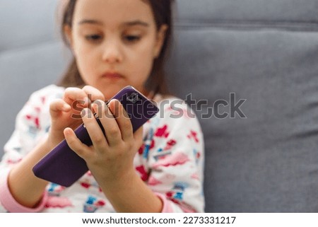 Beautiful little girl playing game or watching video on smartphone mobile. Girl watching cartoons or browsing internet, copy space. Side view portrait of little girl using smartphone while sitting.
