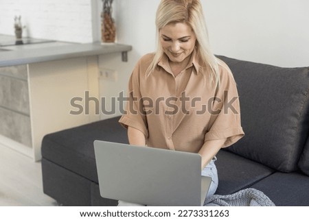 Nice beautiful blonde lady works at the notebook sit down on the sofa at home - check on oline shops for cyber monday sales - technology woman concept for alternative office freelance