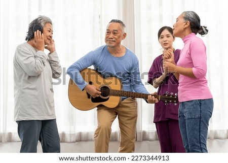 Happy moment with Group of Asian senior man playing guitar and woman singing and dance with fun togetherness in living room at nursing home