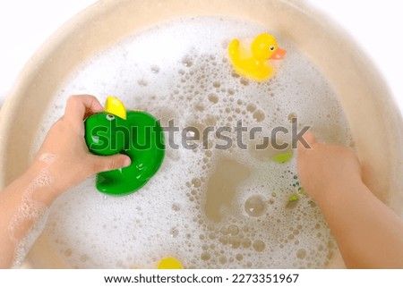 happy child, girl 3 years old plays with rubber green, yellow ducks for swimming, child's toy in soapy foam, concept of bathing in bathtub, playing with water, baby hygiene, healthy lifestyle