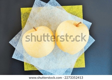 Two Venus type yellow apples on transparent yellow and white Japanese paper on a black background