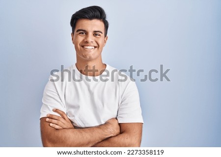 Hispanic man standing over blue background happy face smiling with crossed arms looking at the camera. positive person. 
