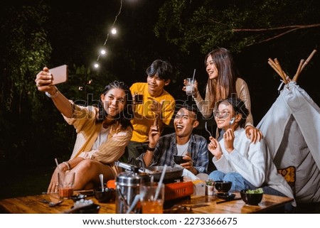 woman in orange stripped shirt holding the phone while taking groufie photo together with all of her friends at the camp site