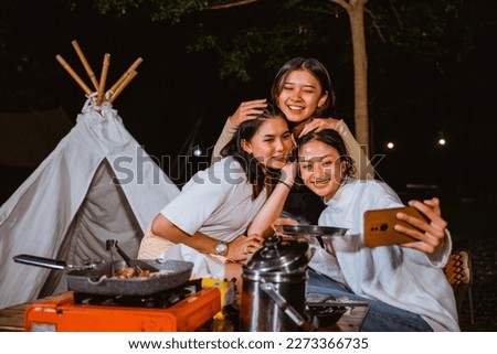 woman in cardigan smiling and embrace her friends heads while taking groufie photo together at the camp site