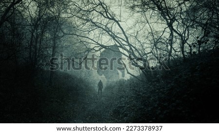 A dark, atmospheric concept of a huge bigfoot monster. Silhouetted in a forest. With a person looking up at them. On a spooky, foggy winters day. Royalty-Free Stock Photo #2273378937
