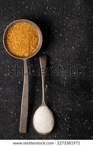 Two old spoons with brown and white sugar on black background. Flat lay. Top view. Food concept. Dark mood food photography.