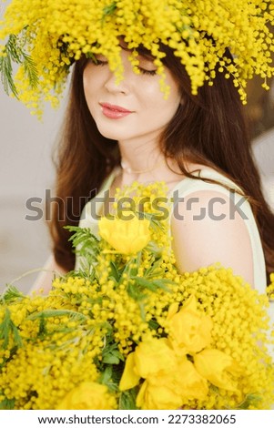 beautiful gentle young woman brunette with a bouquet and in a wreath of mimosa. the concept of femininity and tenderness. cosmetics and clothing for women.